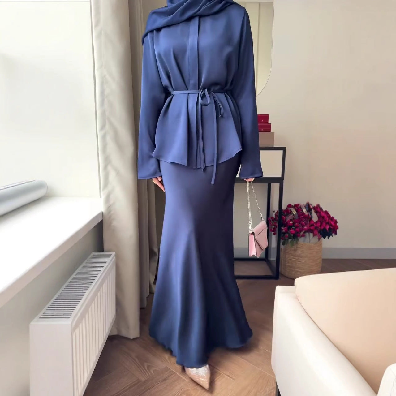 Die Kleidung ist im modischen Modest-Fashion-Stil gehalten, kombiniert mit einem braunen Hijab und einem schmalen Taillengürtel.