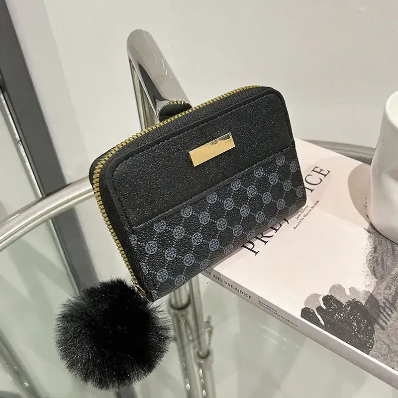Schwarze Damen Geldbörse mit goldenen Details, Zipper, Muster und schwarzem Pompon, stilvoll, modern.