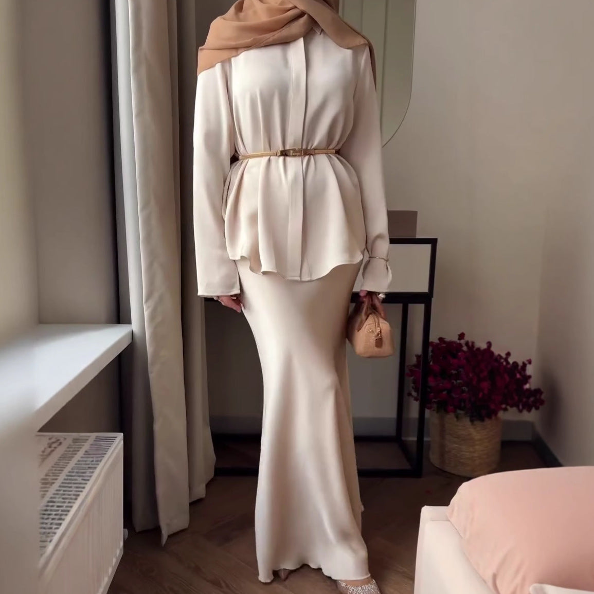 Die Kleidung ist im modischen Modest-Fashion-Stil gehalten, kombiniert mit einem braunen Hijab und einem schmalen Taillengürtel.